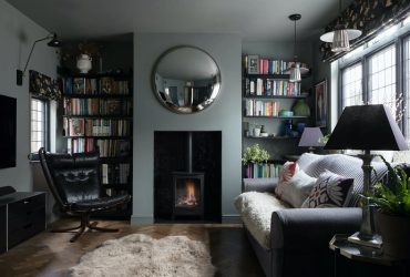 Cozy living room with a wood-burning stove, circular mirror, and bookshelves on both sides.