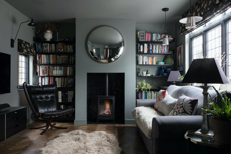 Cozy living room with a wood-burning stove, circular mirror, and bookshelves on both sides.