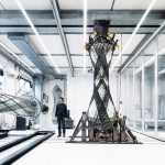 Engineer stands beside a large carbon-fiber wing section mounted on a testing rig in a modern lab interior.