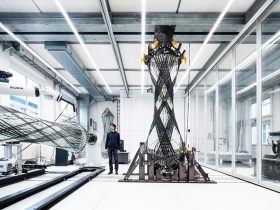 Engineer stands beside a large carbon-fiber wing section mounted on a testing rig in a modern lab interior.