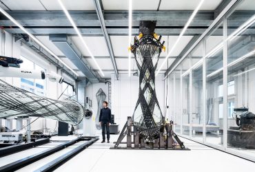 Engineer stands beside a large carbon-fiber wing section mounted on a testing rig in a modern lab interior.