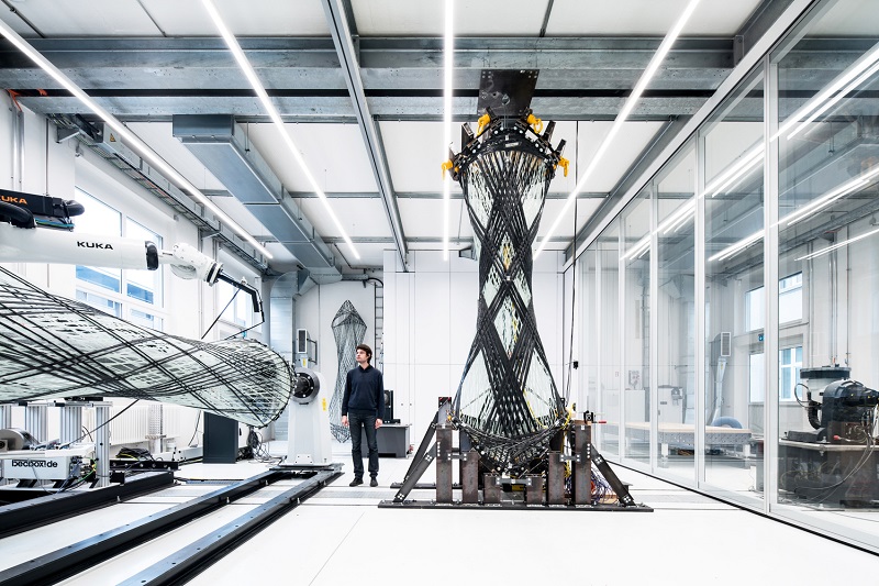 Engineer stands beside a large carbon-fiber wing section mounted on a testing rig in a modern lab interior.